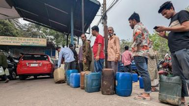 Motorists wait in line to purchase fuel at a petrol station in the Mohammadpur area of Dhaka, Bangladesh. Several people are standing in a queue with various petrol cans waiting to be filled