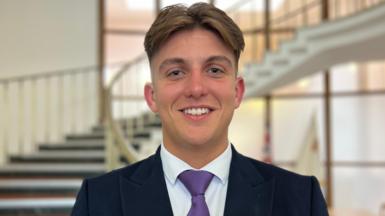 George Finch wears a purple tie and smiles at the camera.