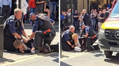 Officers make an arrest in a crowded street with a woman on the ground pinned by two officers.