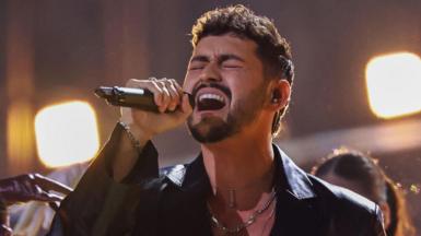 Noam Bettan sings on stage passionately while holding a microphone.