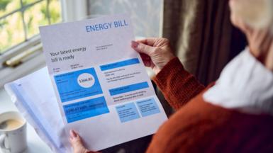Woman looks at paper energy bill near a window.