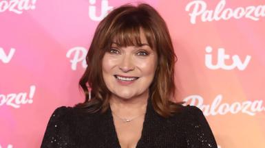 Lorraine Kelly in black sparkle dress in front of a pink branded background covered in logos