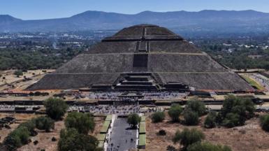 A big pyramid seen from a distance with mountains in the background, and groups of people in the foreground