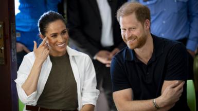 The Duke and Duchess of Sussex siting next to each other smiling at something.