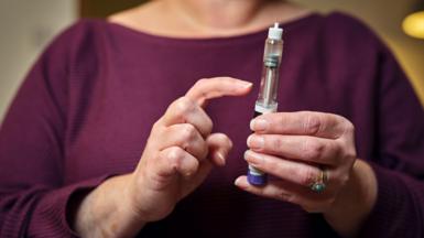 A woman in a burgandy top holds a weight loss injection pen
