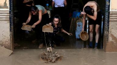 A group of men and women use bowls and other utensils to clean mud out of a large doorway