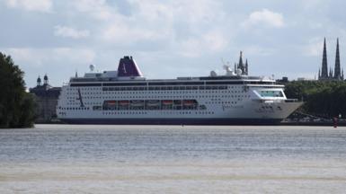 A large cruise ship, which is white, with purple and green markings, is seen docked at a port 