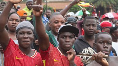 A group of youngsters stand in a crowd; some raise their fists and wave flags.