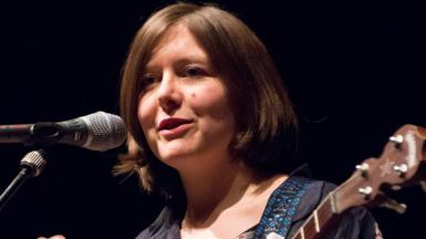 Emily Portman holding a guitar and speaking into a microphone on stage
