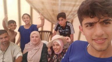 A selfie taken by Sha'aban al-Dalou showing him and his family. He is a young man of 19 in a blue t-shirt, standing in the foreground, with six relatives aged from childhood to middle age smiling behind him. Some of the children are making thumbs-up gestures.