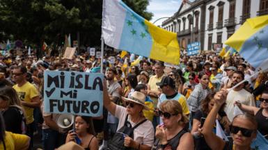 People hold signs and flags while protesting against tourism in the Canary Islands.