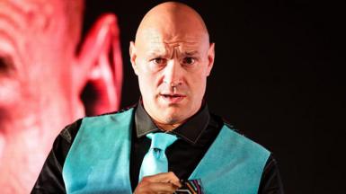 Tyson Fury looks on in a neon blue waistcoat and tie