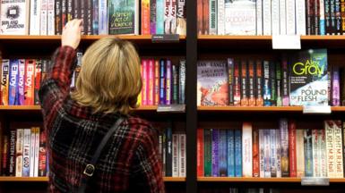 A woman reaches up to a bookshelf in a Waterstones bookstore in Cambridge.
