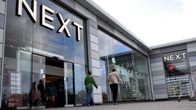 A Next store is seen with the logo looming large over passers-by as they walk outside the storefront on a sunny-cloudy day in Basildon in October.
