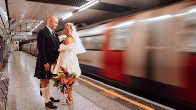 Thomas and Paige Mackintosh stand on a Jubilee line platform at Baker street as a tube carriage whizzes by them on their wedding day.