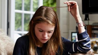 A girl twiddles a lock of hair while looking at her iPhone