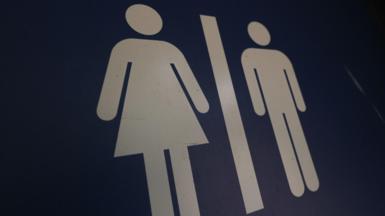 A blue gender neutral toilet sign, showing an image of a woman on the left and the image of a man on the right.