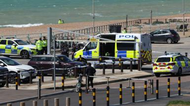 Police vehicles and officers in the Black Rock car park on Madeira Drive after the bodies of three women were recovered from the sea in Brighton. The car park is next to a pebble beach, where two more officers are standing in the distance