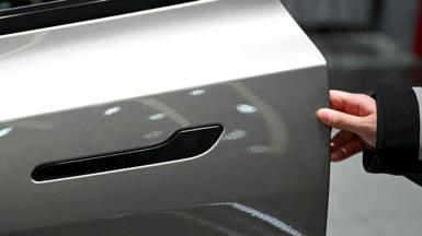 A customer inspects the minimalistic hidden door handles on an electric car in a showroom.