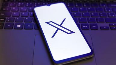 X logo displayed on a smartphone lying on a laptop keyboard