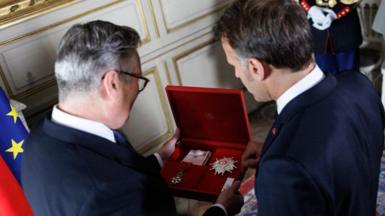Sir Keir Starmer and Emmanuel Macron pictured from behind as they look at the opened red-velvet box Starmer is holding in his hands with the decoration visible inside