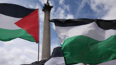 Palestinian flags fly in front of Nelson's Column and a cloudy blue sky in the background during a demonstration in support of Palestine Action in Trafalgar Square, London.