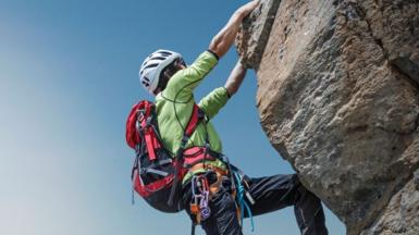 Stock image of a female climber wearing a backpack hanging onto a rock