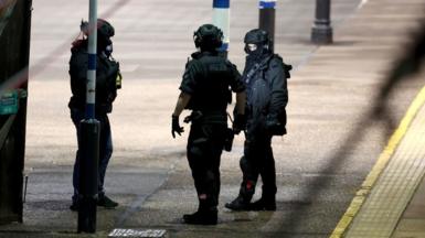 Three specially trained officers dressed in dark clothing, helmets and gloves stand on a train station platform