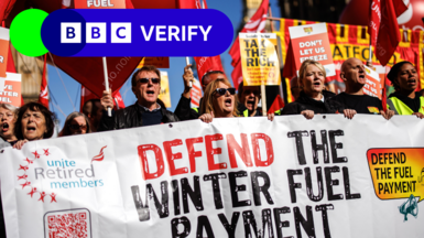 Demonstration in London on 7 October against the means-testing of Winter Fuel Payments. Six people are seen holding a sign saying "Defend the Winter Fuel Payment" with other signs saying "Tax the rich" and "Don't let us freeze". The BBC Verify logo is in the top left corner of the image.