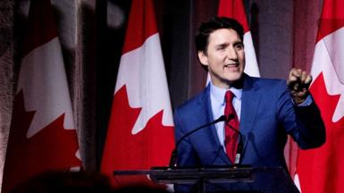 Canada’s Prime Minister Justin Trudeau speaks on stage at a rally with several Canadian national flags hung in the background