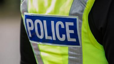 The back of a police officer. They are wearing a yellow high-vis jacket with "POLICE" written on in white within a blue rectangle.