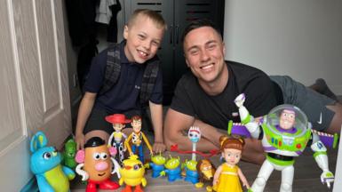 A child and his father lying at a doorstep with an array of toys from the Toy Story film franchise
