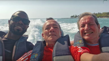Yostin Mosquera, 34, Paul Longworth, 71 and Albert Alfonso, 62, on a boat in Colombia. Mr Longworth and Mr Alfonso are both wearing red T-shirts whereas Mr Mosquera has a black T-shirt on. In the background is the sea and land to the right.