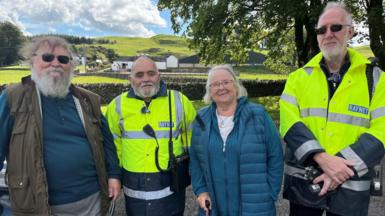 An up-to-date image of the four friends, Ross, Tom, Anne and William. A field and a farm are behind the row of four and the sun is shining.