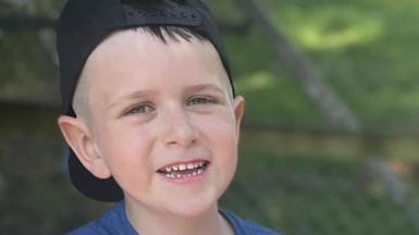 Picture of a smiling boy wearing a baseball cap back to front.