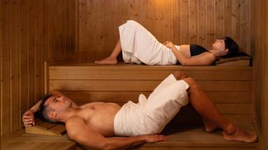 Couple lying on levels in a wooden sauna 