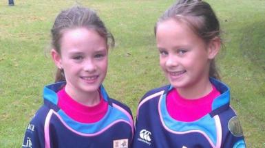 An old image showing Ffion and Celyn standing on a field smiling at camera in rugby kit. 