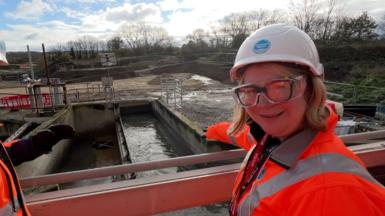 A woman in a hi-viz coat and hard hat stands above a sewage plant.