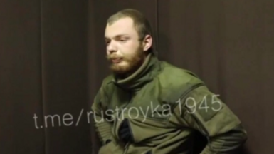 A man believed to be James Scott Rhys Anderson, 22, a former British Army soldier captured while fighting for Ukraine, is seen wearing green military clothing and sat in front of a plain brown background. 