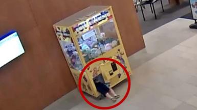 Child is climbing inside a claw machine.