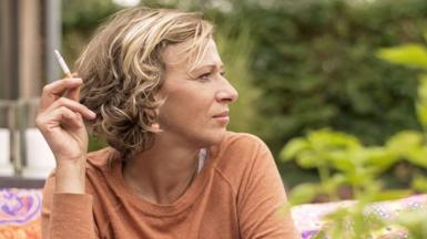 A woman sits outside and smokes