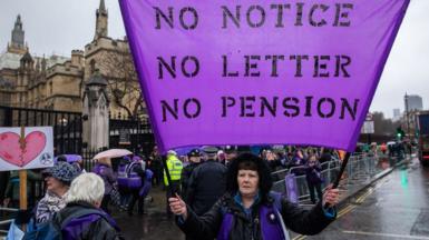 A Waspi campaigner holds a purple banner which reads "No notice, No letter, No pension" during a protest outside the Houses of Parliament on International Women's Day in 2023