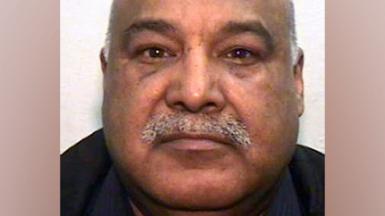 A mugshot of an Asian man in his 60s, with a grey moustache and bald head. He is looking into the camera.