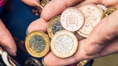 Very close up on a hand holding one pound coins as well as one and two pence pieces.