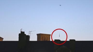Drone dropping package behind wall - the package is circled in red