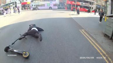 An e-scooter rider, dressed in black, lying on the floor in the middle of road in Nottingham after having crashed.