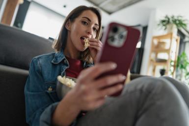 A young woman browsing on her smartphone while eating popcorn