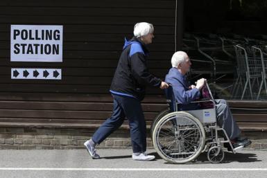 A man in a wheelchair being pushed towards into a polling station