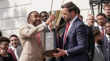 JD Vance holds a trophy with the help of another man, as a crowd watches