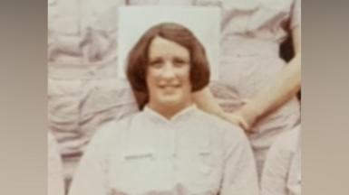 A historic sepia photograph of a female nurse in white uniform smiling at the camera.